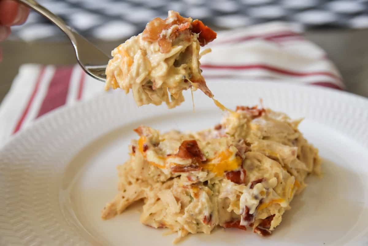 A serving of slow cooker crack chicken on a white plate, with a bite being lifted by a fork.