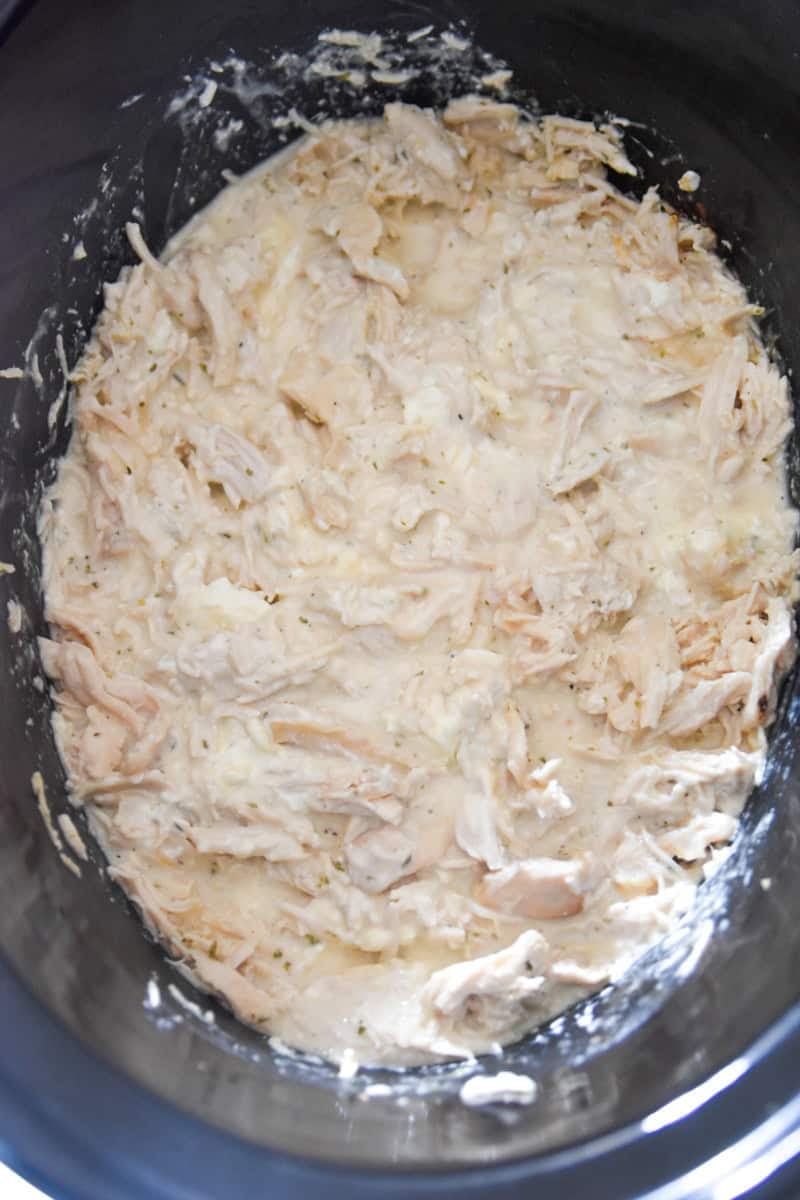 Slow-cooked chicken with melted cream cheese and seasonings, beginning to be stirred together.