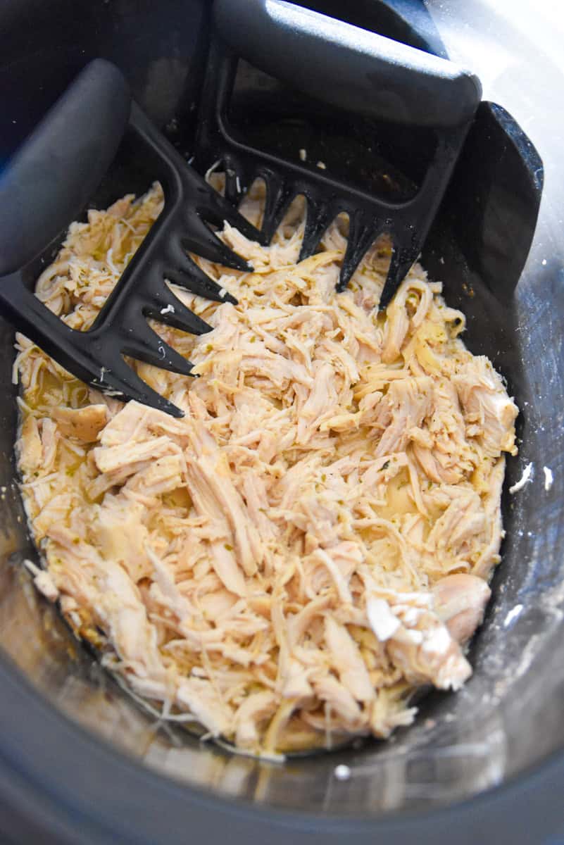 Chicken being shredded inside a slow cooker using black meat claws.