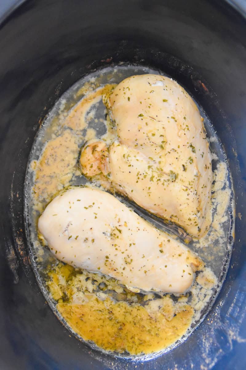 Two seasoned chicken breasts cooked and resting in broth at the bottom of a slow cooker.