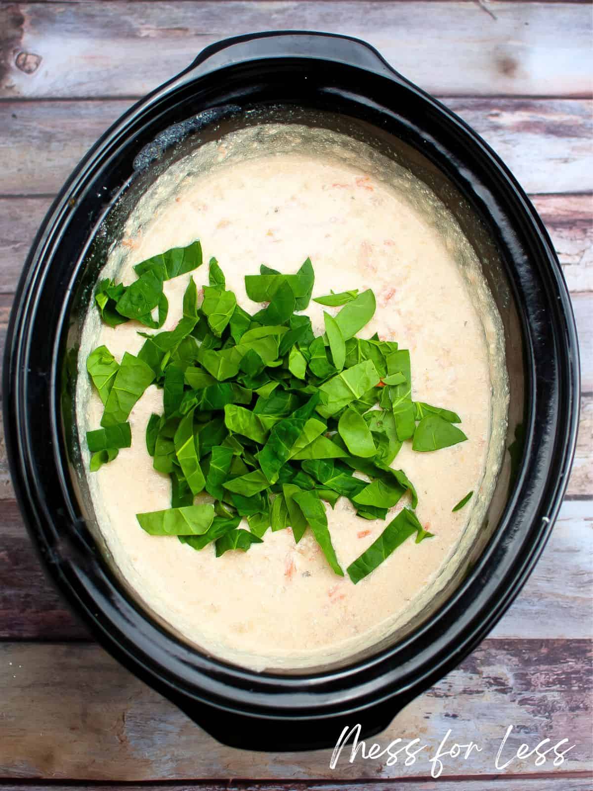 Soup in slow cooker with spinach leaves