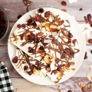 White chocolate bark with almonds and cranberries drizzled with chocolate on white plate