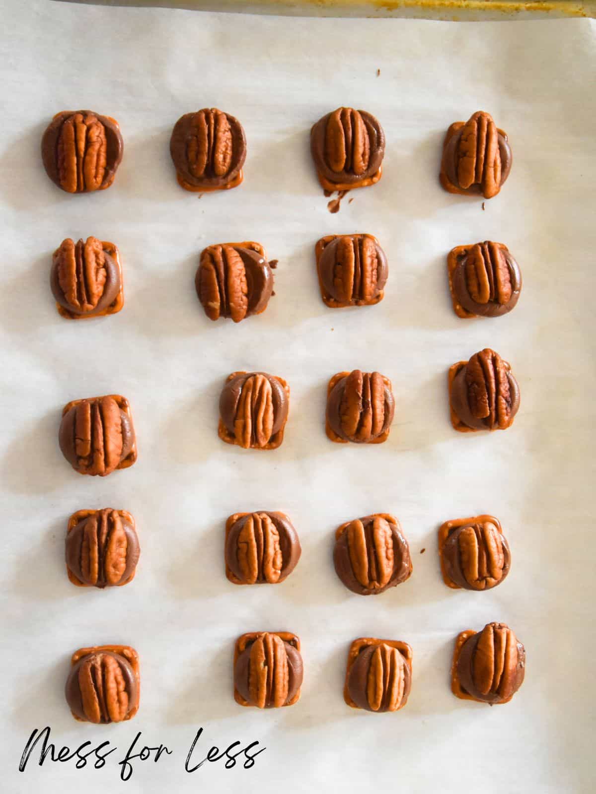 square pretzels with rolo and pecans on them on cookie sheet