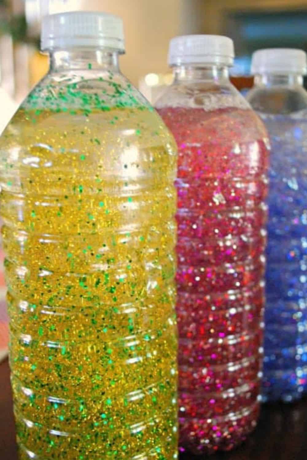 Three transparent plastic bottles filled with colorful glitter and liquid are perfect for sensory activities for preschoolers. The left bottle contains green and gold glitter, the middle one has red and pink glitter, and the right bottle features blue and purple glitter.