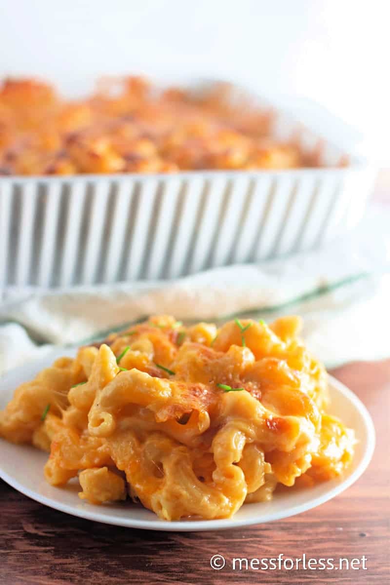 Close-up of a serving of baked macaroni and cheese on a plate with crispy golden topping, with a full baking dish in the background.
