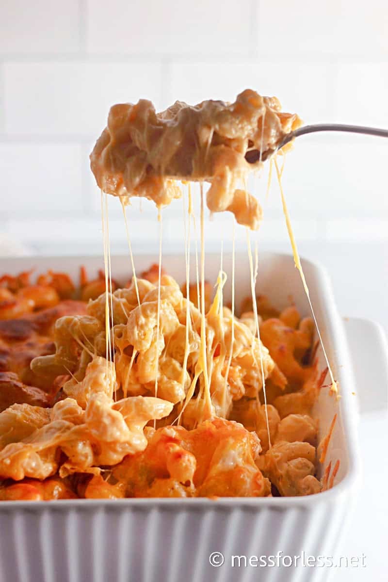 Spoon lifting a gooey serving of baked mac and cheese from the pan, with melted cheese stretching in long strings.