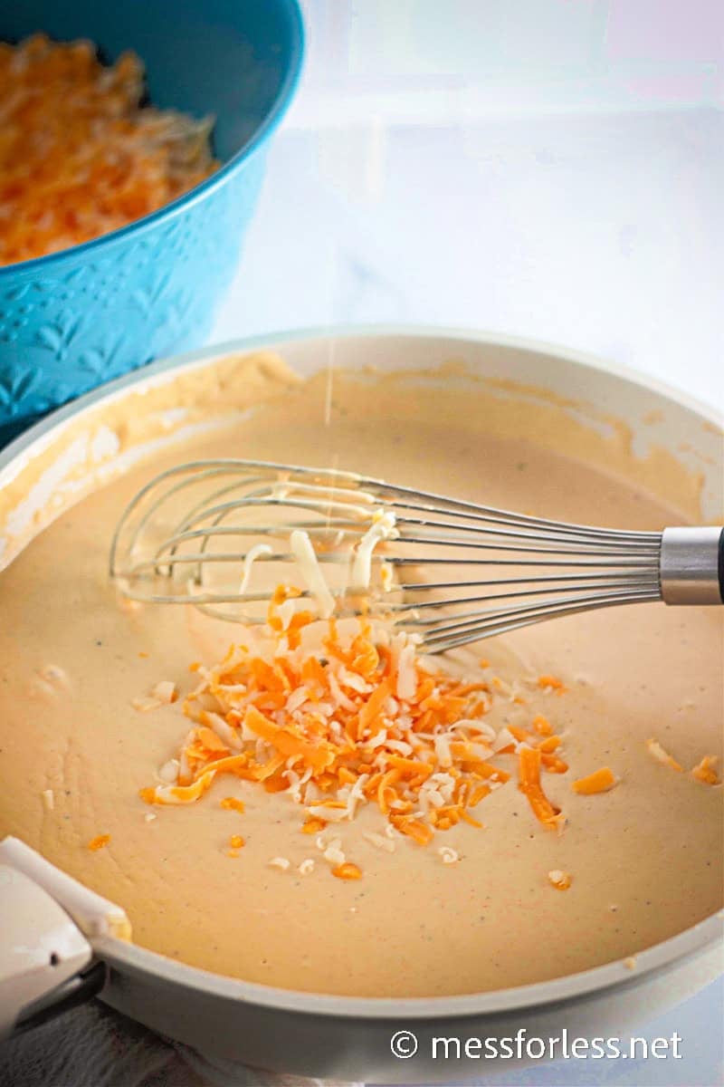 Shredded cheese being whisked into a creamy homemade cheese sauce for baked macaroni and cheese.