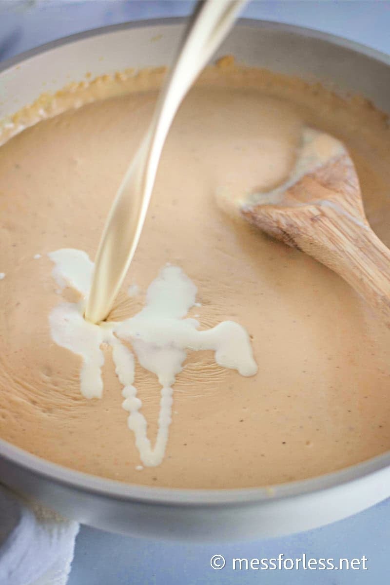 Cream being poured into a roux to create a smooth cheese sauce for baked mac and cheese.