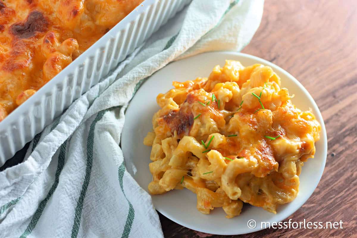 Golden, bubbly baked macaroni and cheese served on a white plate with chopped herbs.