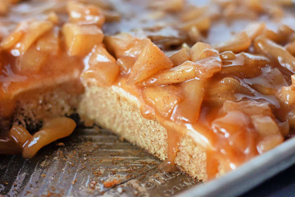 Close-up of a sliced caramel apple cake with a gooey apple topping on a metal tray.