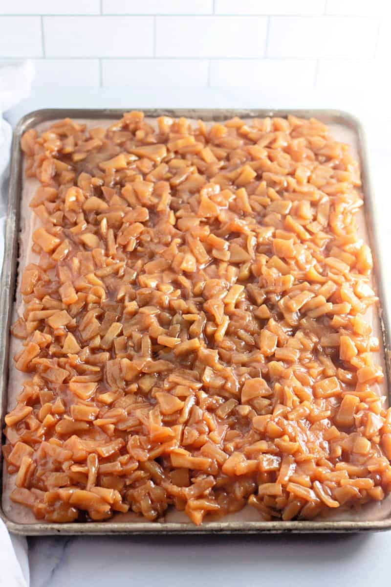 A baking sheet filled with evenly spread caramelized diced apples, perfect for your next apple cake recipe.