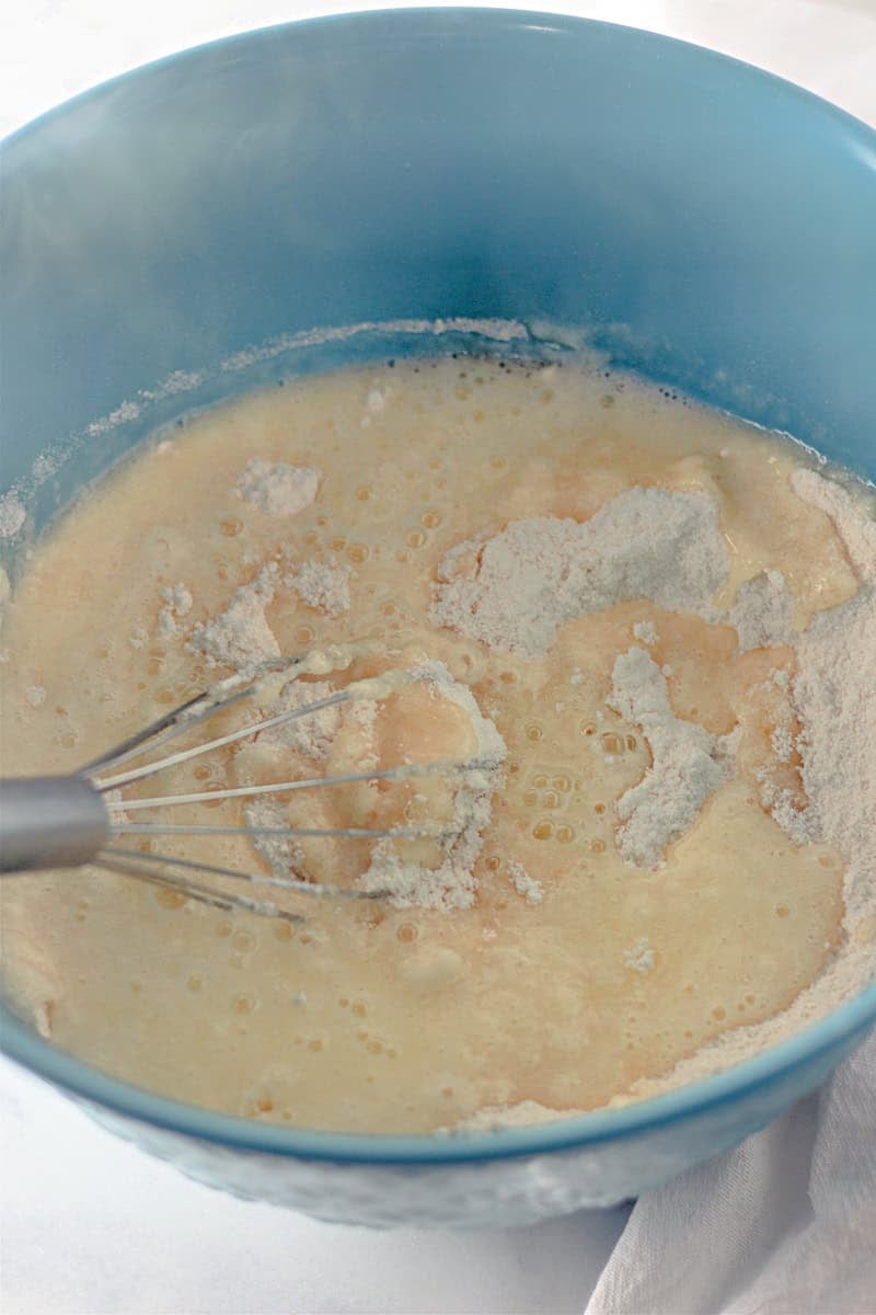Whisking the batter for our caramel cake recipe in a large blue bowl on a white surface.