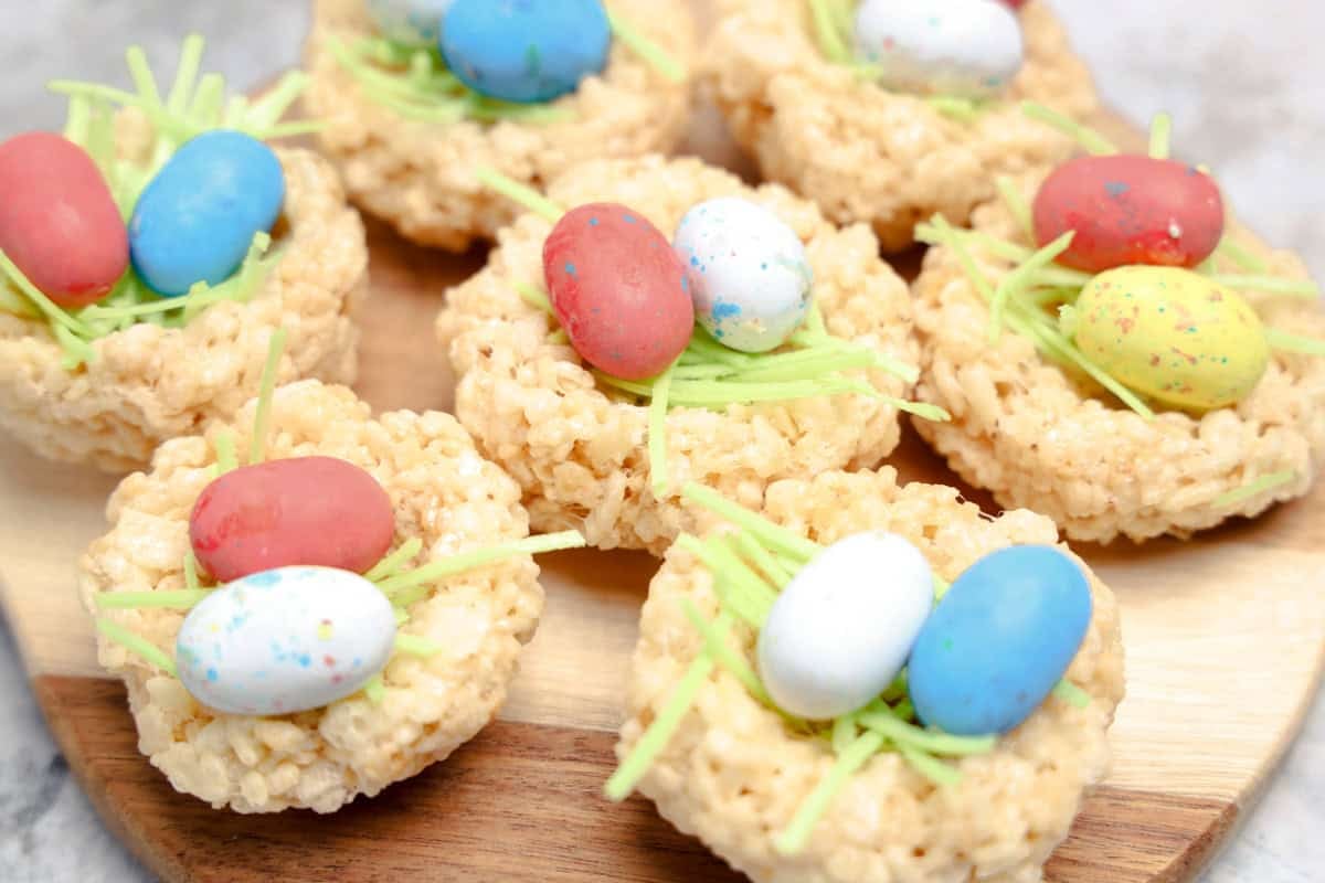 Close-up of Easter nest Rice Krispie treats topped with edible green grass and colorful candy eggs, arranged on a wooden board.