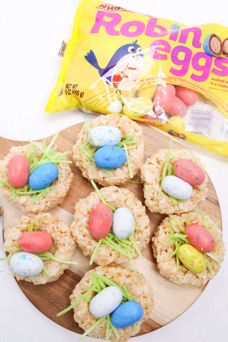 Festive Easter Rice Krispie nests topped with speckled candy eggs, shown with a bag of Robin Eggs candy in the background.