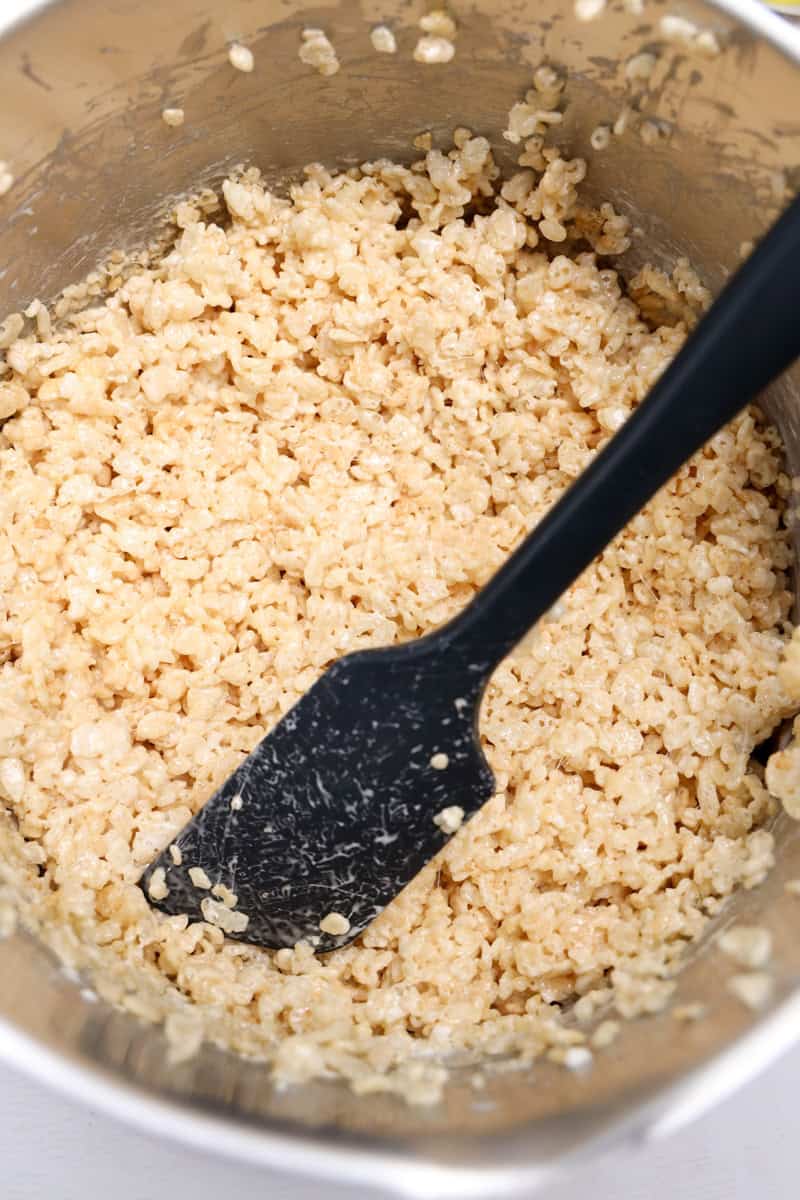 Bowl of freshly mixed Rice Krispie treat mixture being stirred with a black spatula, ready to be shaped into nests.