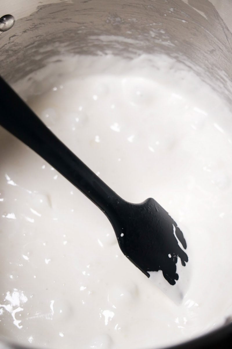Creamy, melted marshmallow mixture in a mixing bowl with a black spatula, the gooey base for Rice Krispie treats.