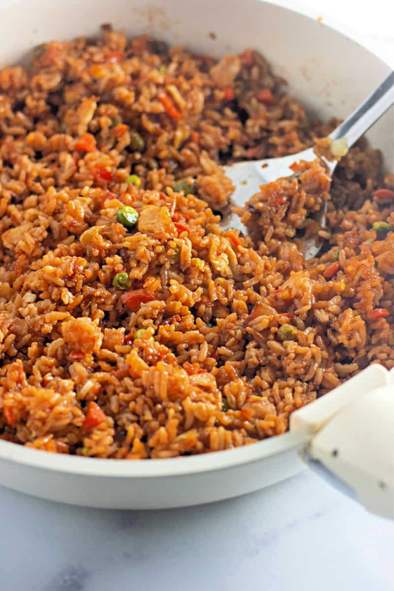 fried rice with veggies in a white pan with a spatula