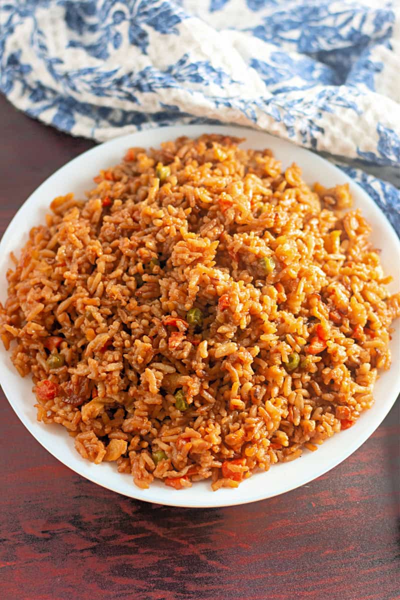 Plate of easy fried rice with vibrant vegetables on a wooden table, complemented by a blue and white cloth in the background.