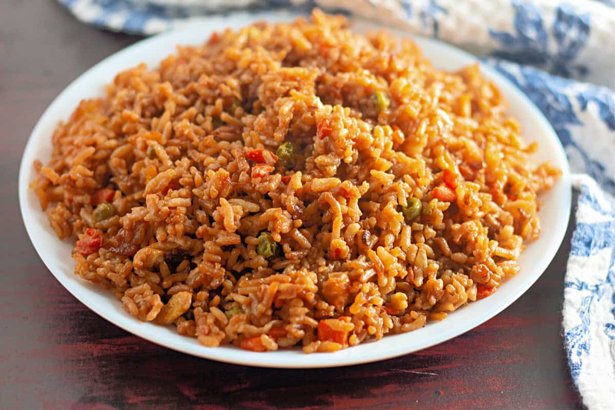 Fried rice with peas and peppers on a wooden table with a white and blue flowered place mat in the background