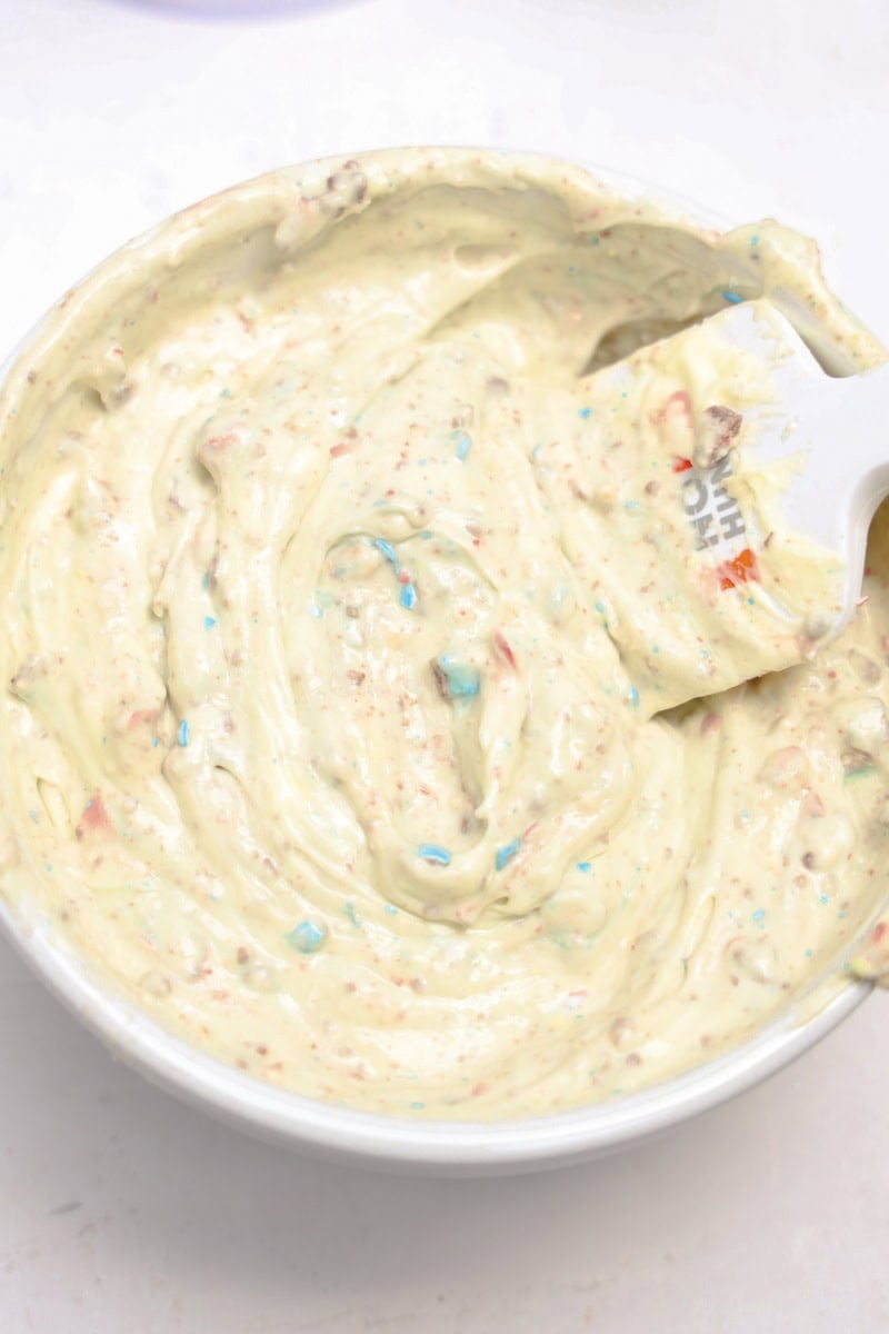 A bowl of colorful sprinkle cake batter reminiscent of Robins Egg Easter Dip being gently stirred with a white spatula.