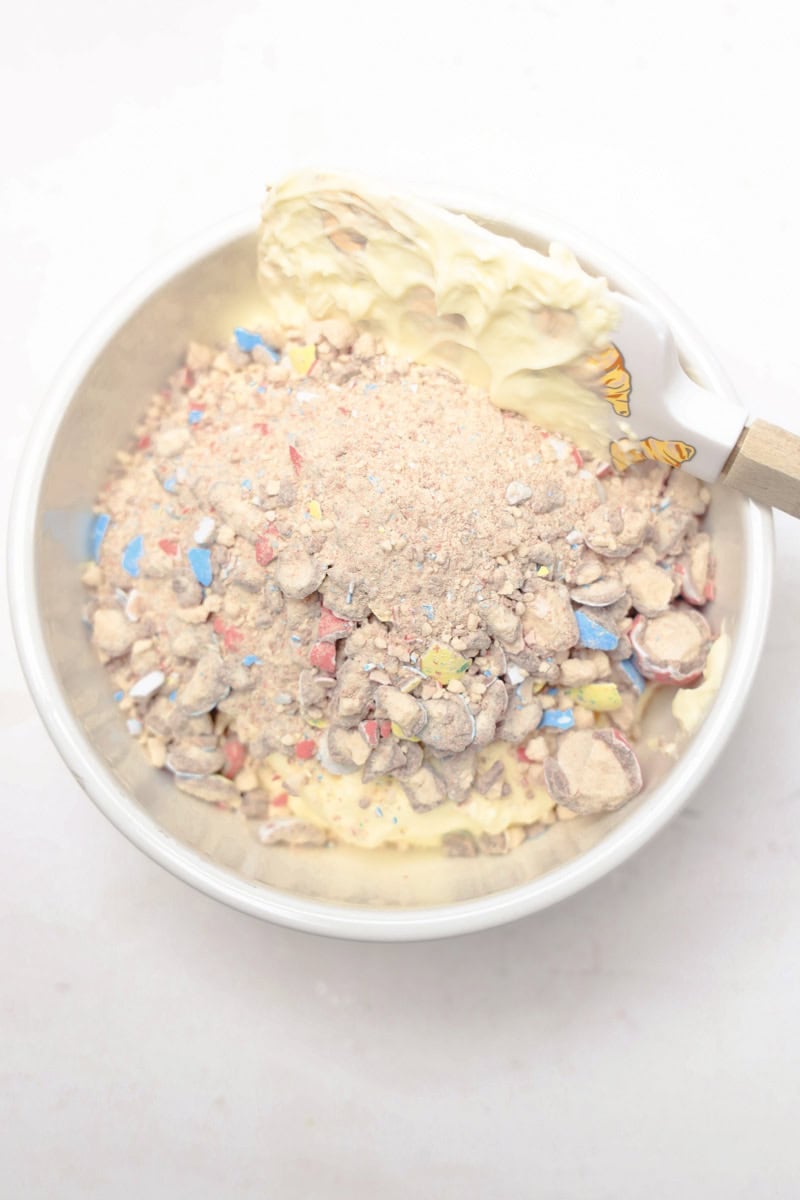A vibrant bowl of crushed colorful candy and white chocolate is gently mixed with a spatula, creating the delightful Robins Egg Easter Dip.