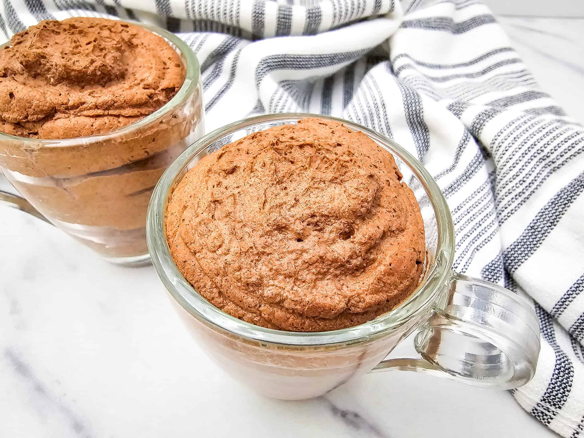 Two glass mugs filled with rich 3 ingredient chocolate mug cake, with a striped towel in the background.