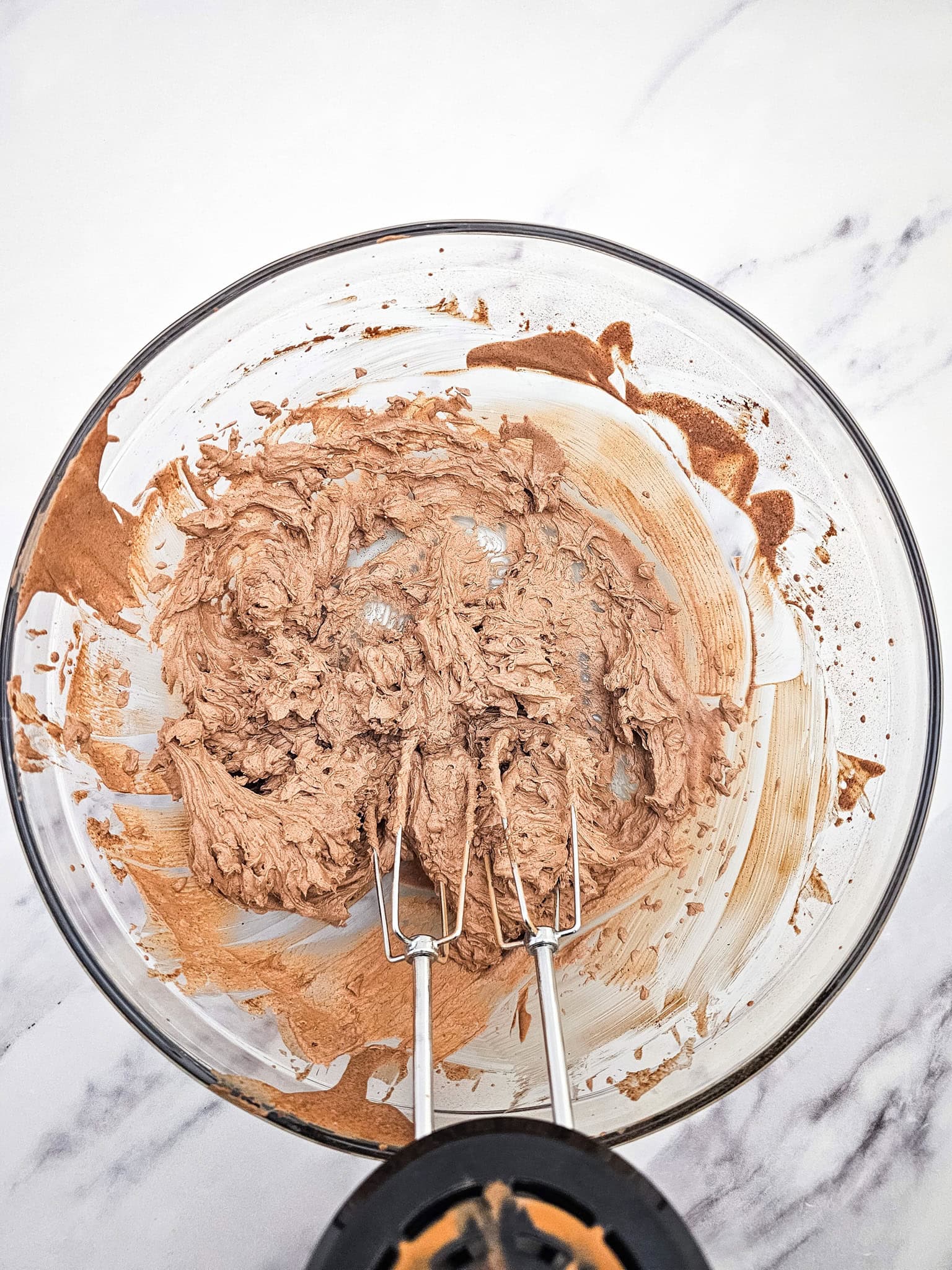 Chocolate cake batter being mixed in a clear glass bowl with an electric hand mixer on a white surface, perfect for creating a rich low carb mousse or an easy 3 ingredient keto dessert.