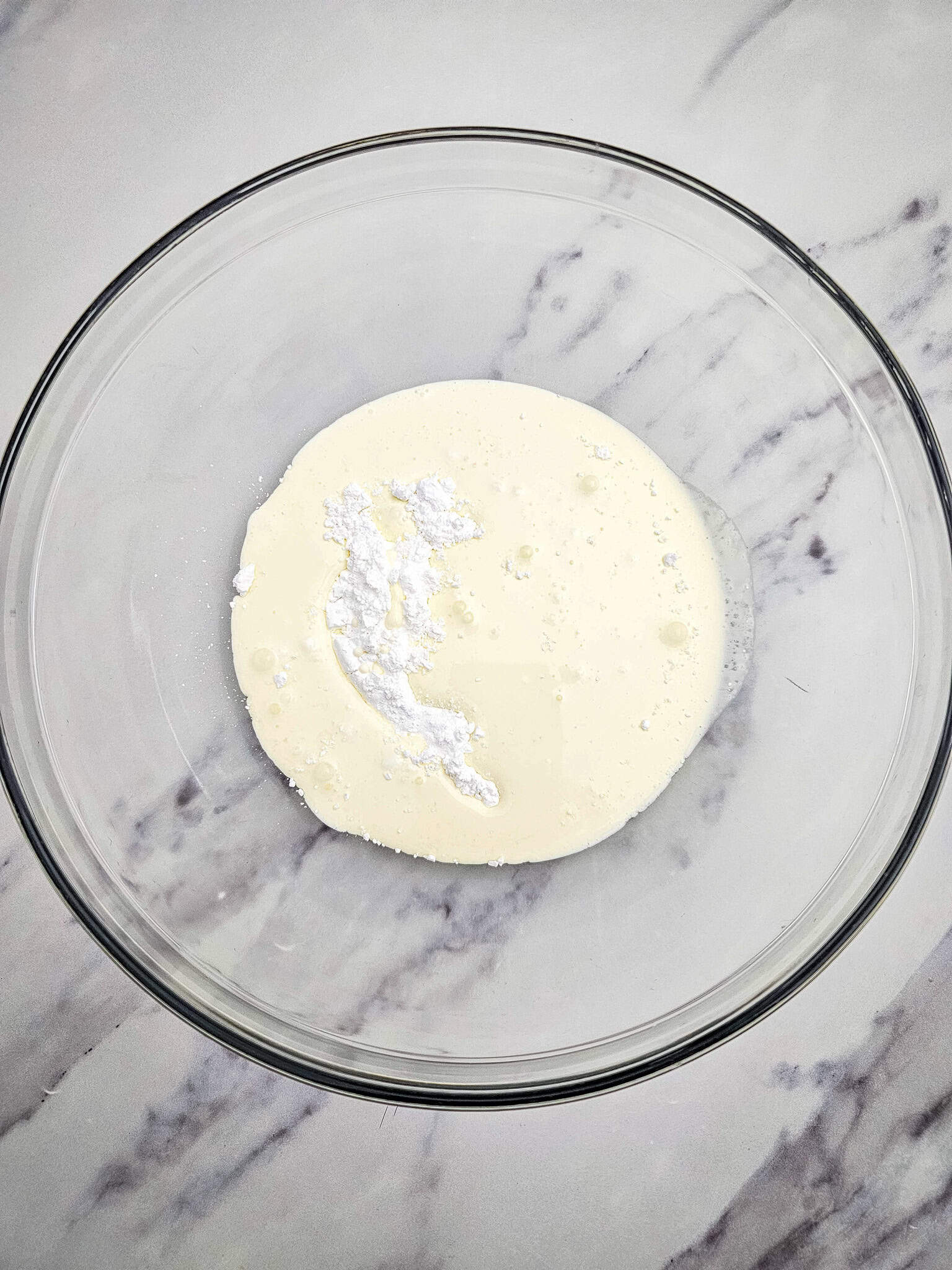 Glass bowl with cream and powdered sugar on a marble surface, ready for mixing this easy 3 ingredient Chocolate Mousse.