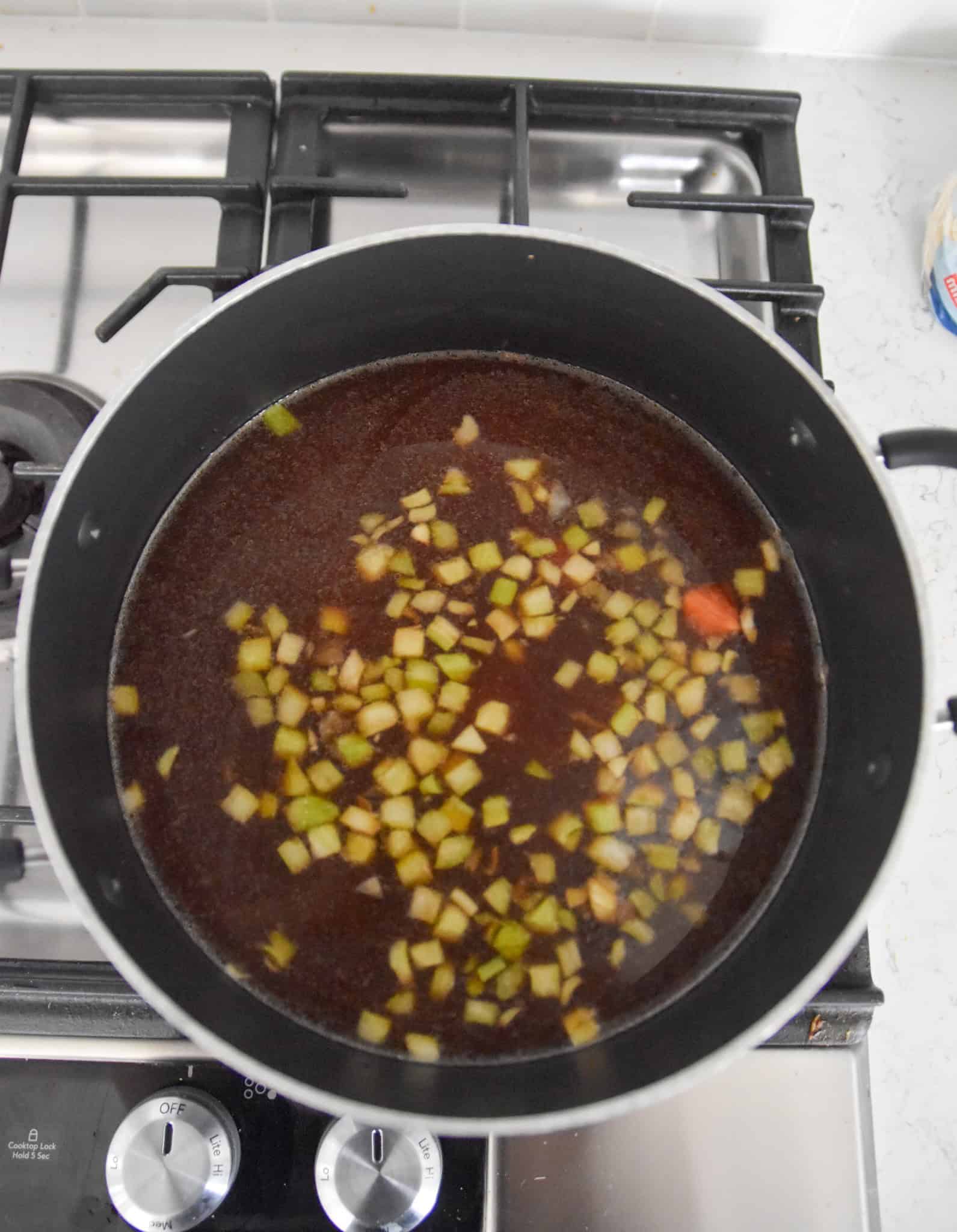 A pot of dark beef soup with chopped celery and carrots simmers on the stovetop