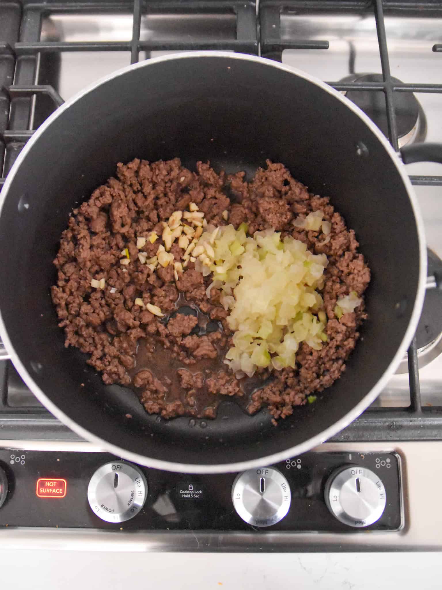 ground beef, chopped onions, and minced garlic simmering in a pot on the stove.