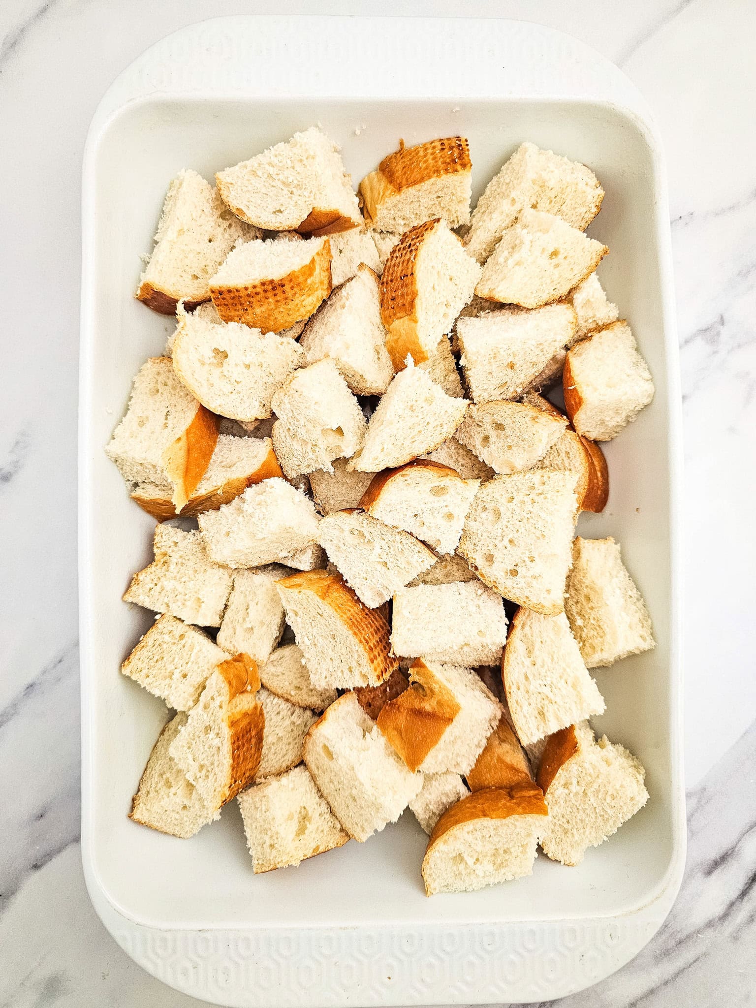 White casserole dish filled with torn bread pieces, forming the base layer for the raspberry French toast bake.