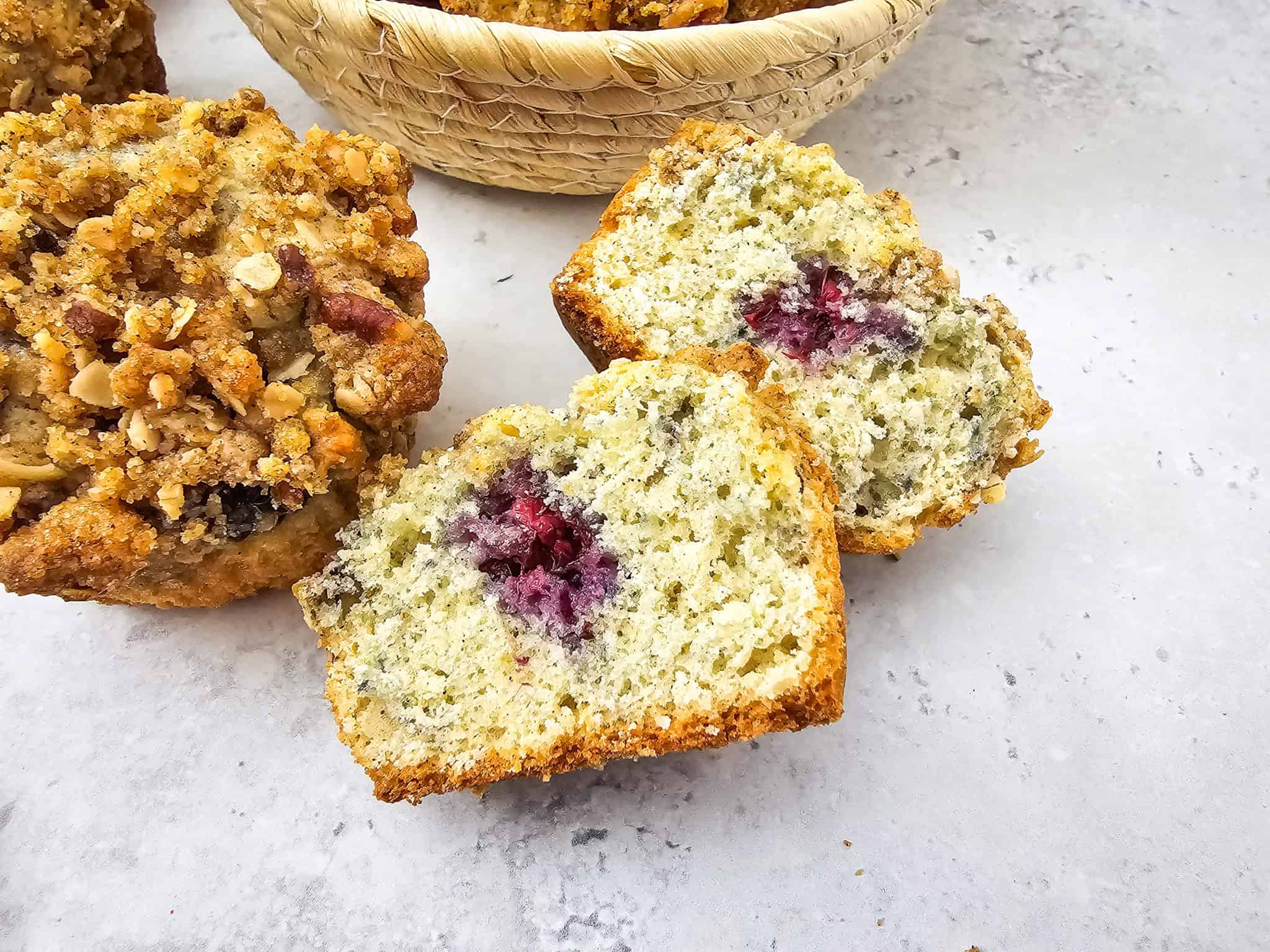 Sliced blackberry muffin with crumb topping, showing a purple berry center, on a light surface