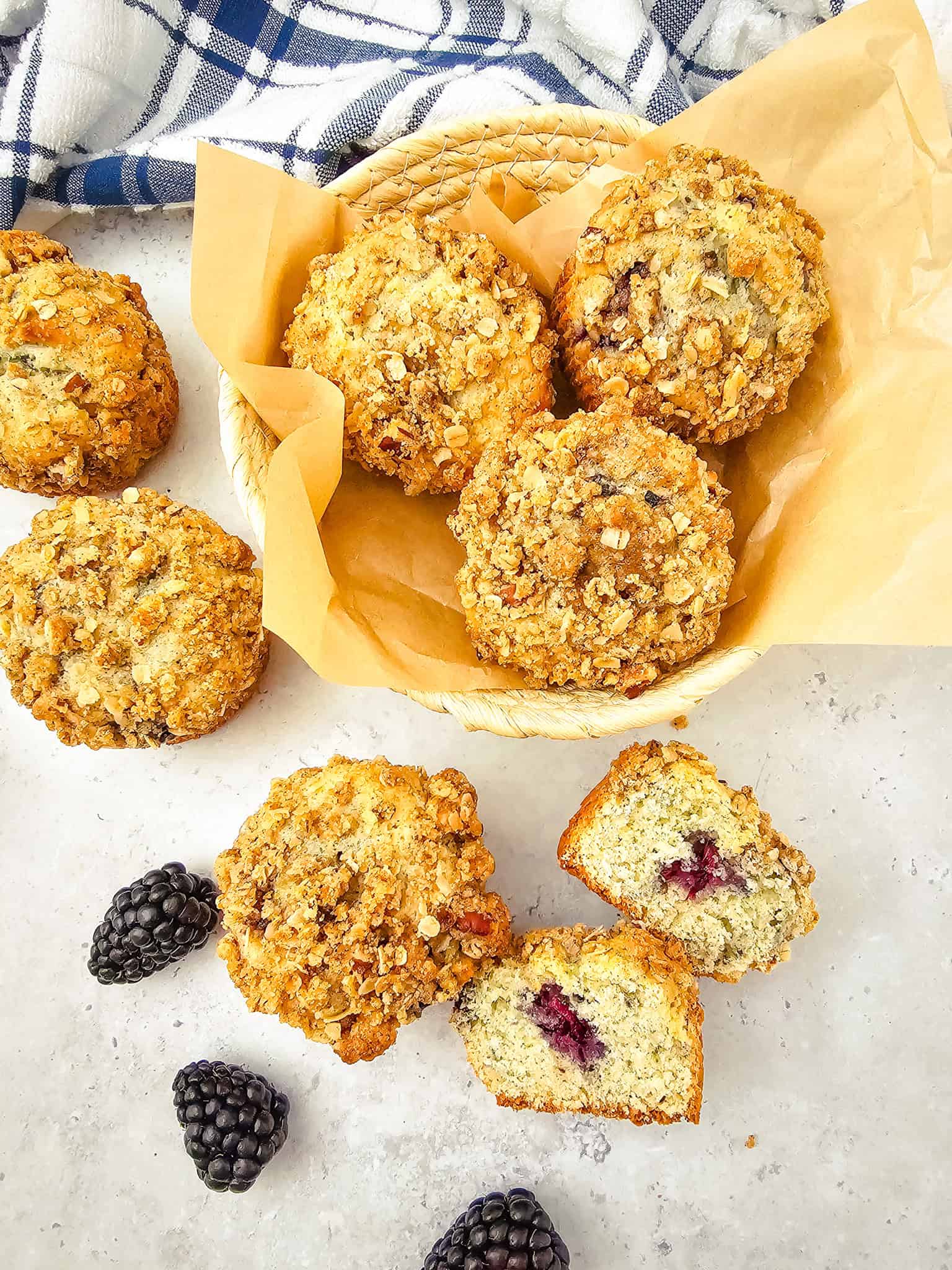 Basket of oat-topped blackberry muffins with fresh blackberries and a cut muffin showing the berry filling