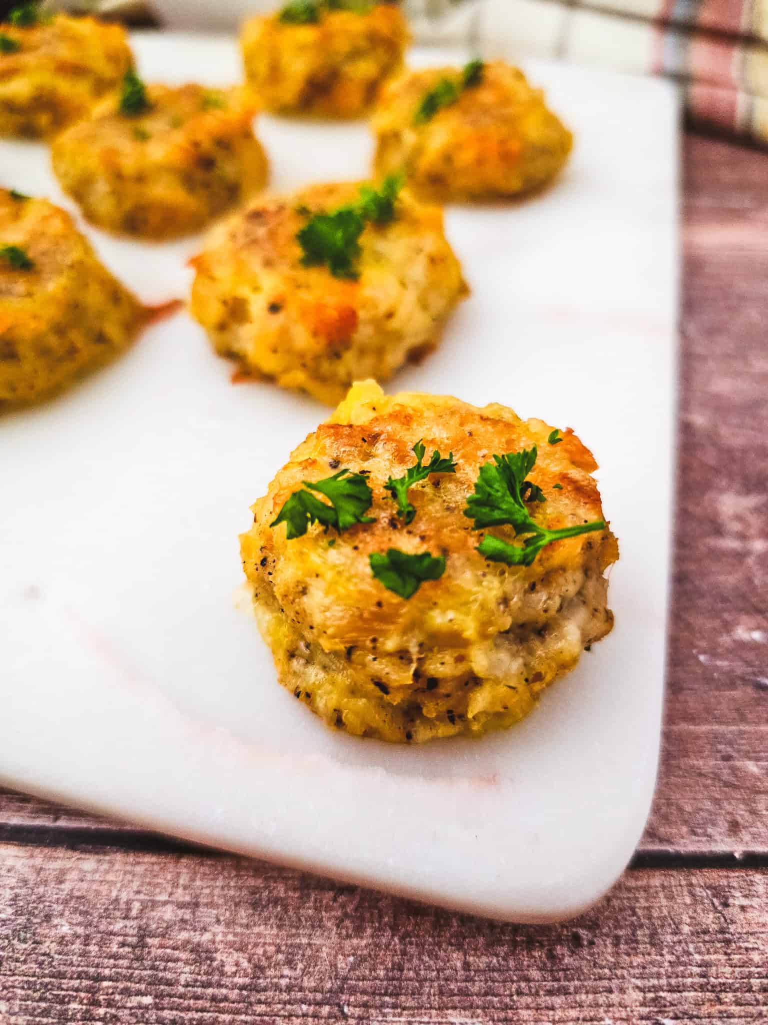 Golden baked keto chicken nuggets garnished with chopped parsley on a white marble surface.