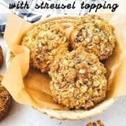A basket of Blackberry Muffins with streusel topping sits on parchment paper, showcasing one muffin cut open in front
