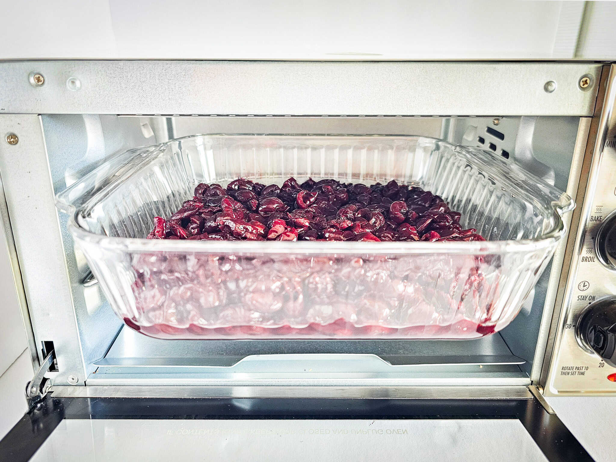 A glass dish with frozen cherries baked into an air fryer dessert inside a toaster oven.