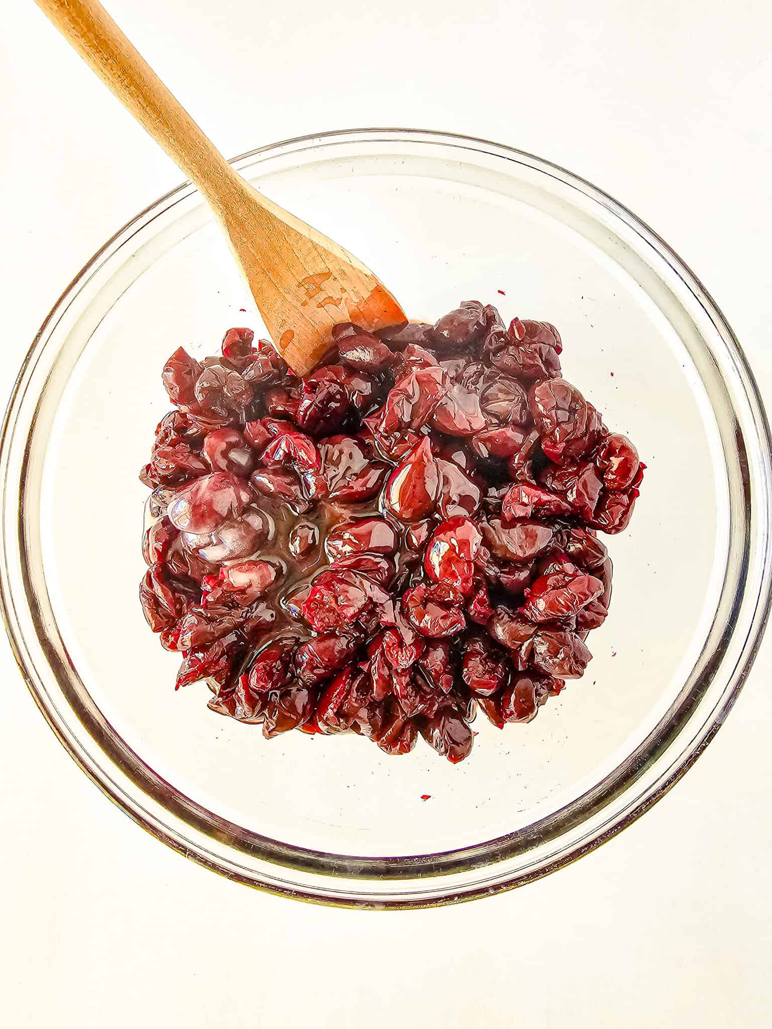 A glass bowl of dried cranberries with a wooden spoon, perfect for topping a cherry crisp or enjoying alongside frozen cherries, set on a white background.