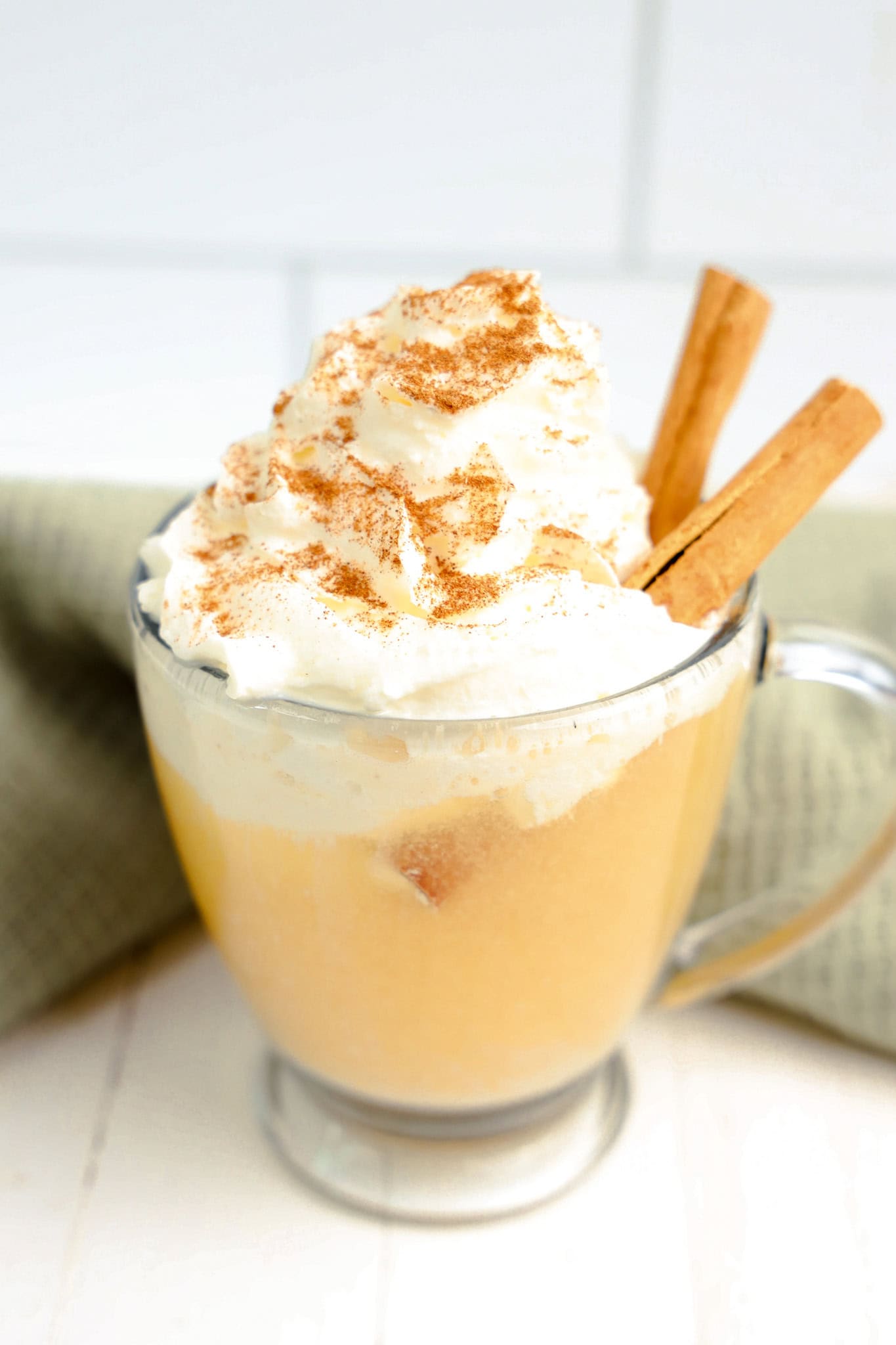 apple cider float in glass with whipped cream and cinnamon sticks
