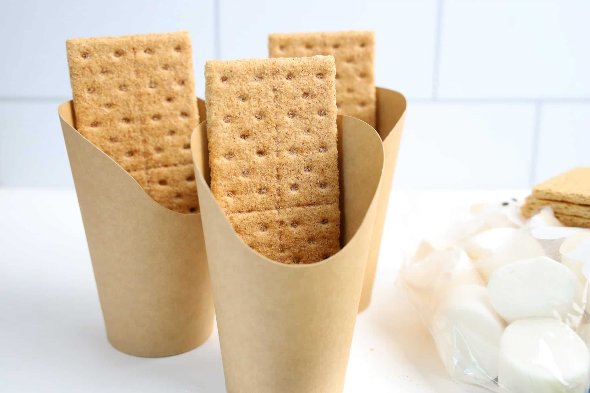 Three paper cups each hold two rectangular graham crackers for Smores Cups