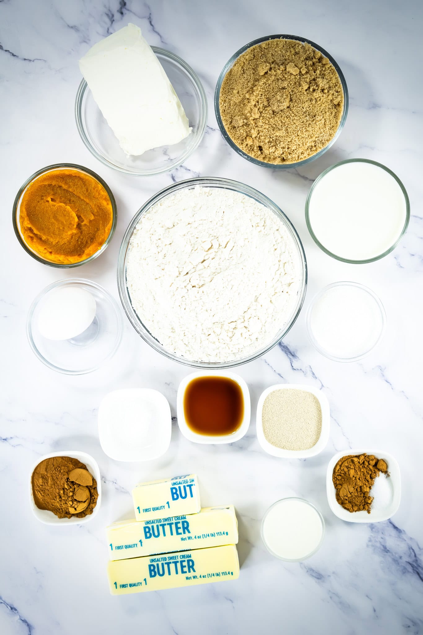 Assorted baking ingredients—flour, butter, pumpkin puree, brown sugar, spices, milk, and more—on a marble surface