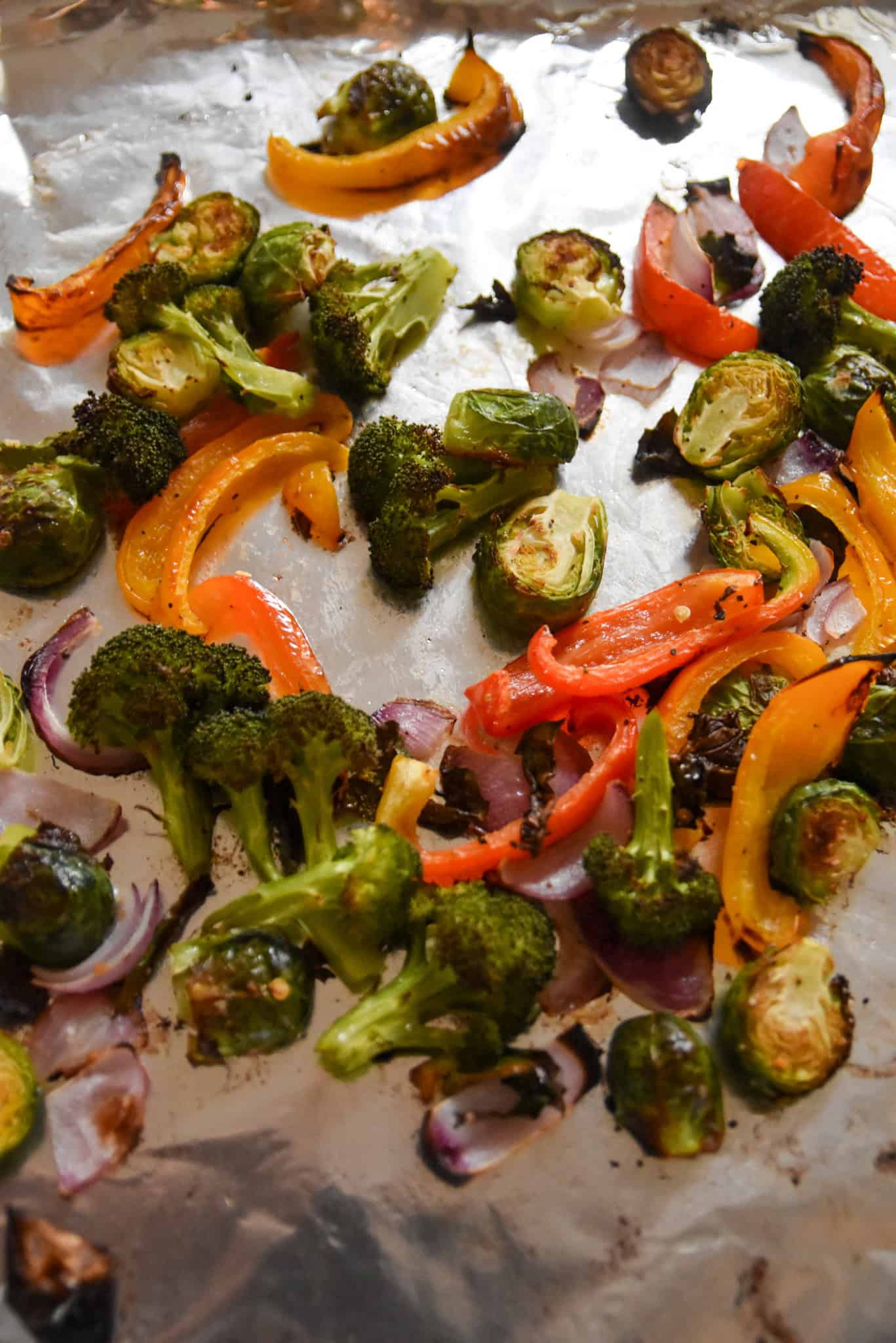 A colorful mix of Sheet Pan Vegetables—broccoli, Brussels sprouts, bell peppers, and onions—perfectly roasted on a foil-lined sheet pan for a delicious side dish.