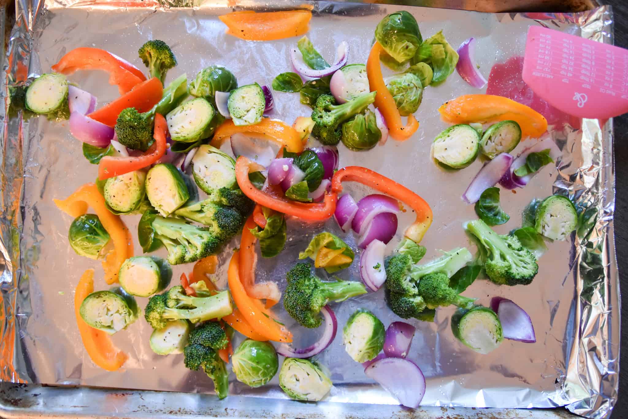 Sheet Pan Roasted Vegetables - broccoli, brussels sprouts, red onion, and bell pepper are arranged on a foil-lined baking sheet, ready for the oven.