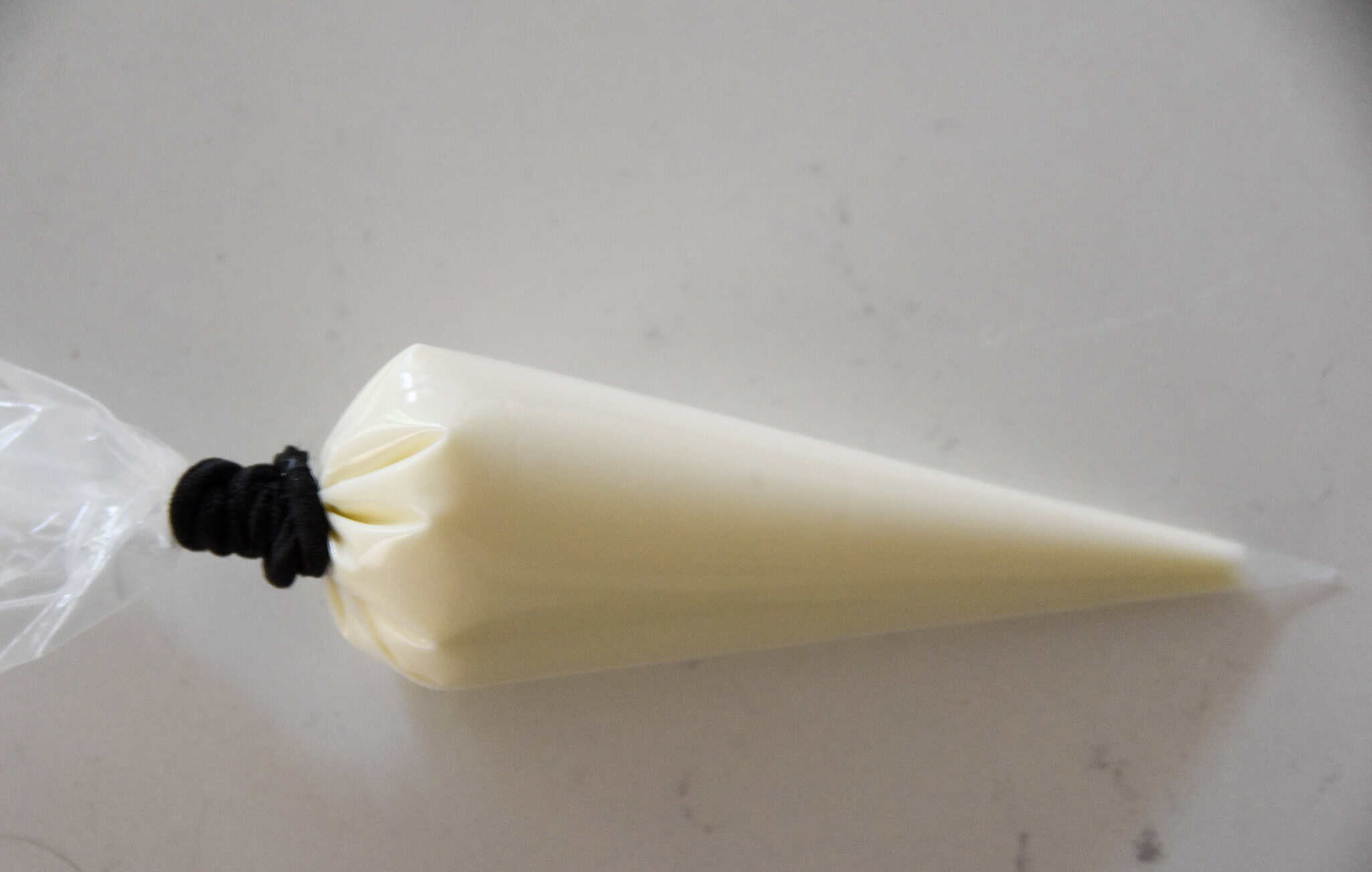 A piping bag filled with white icing, perfect for decorating Mummy Cookies or drizzling over wafer cookies, is closed with a black twist tie on a light surface.