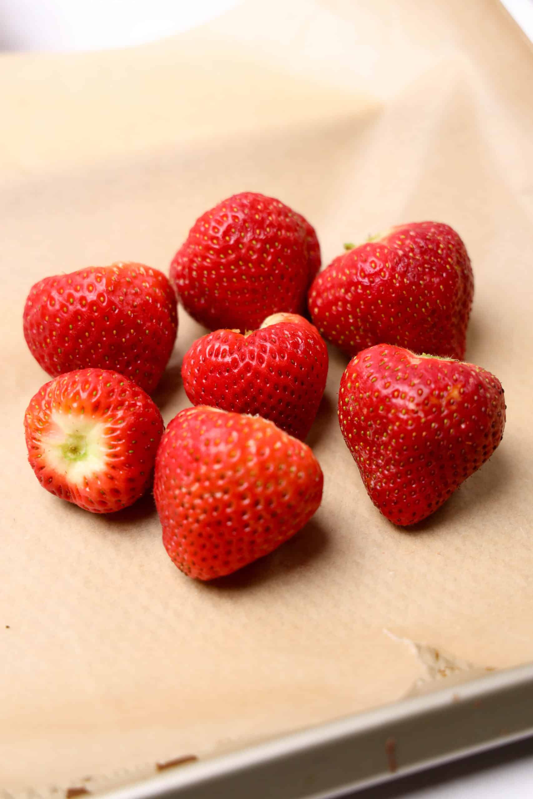 Seven ripe strawberries—perfect for creating Strawberry Acorns or Chocolate Covered Strawberry Acorns—are arranged on a sheet of brown parchment paper.