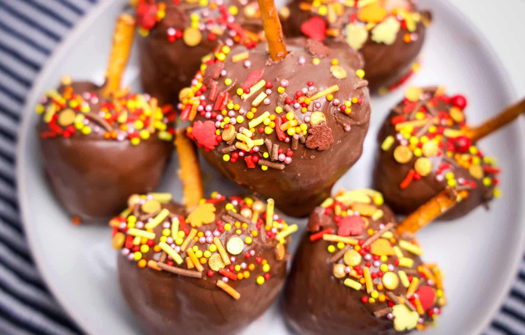 Chocolate Covered Strawberry Acorns and pretzel sticks, topped with colorful sprinkles, are arranged on a white plate for a delightful treat.