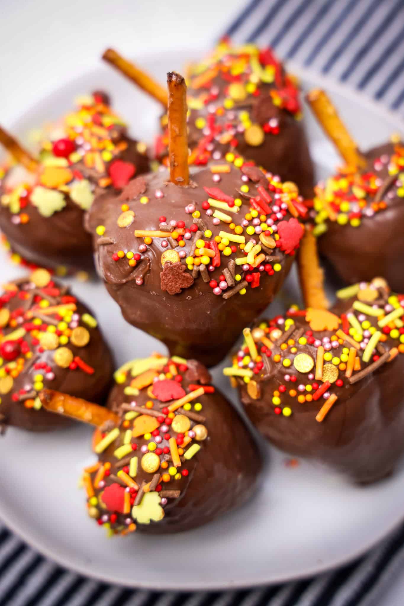 Chocolate-covered strawberries with pretzel sticks, colorful fall-themed sprinkles on a white plate.