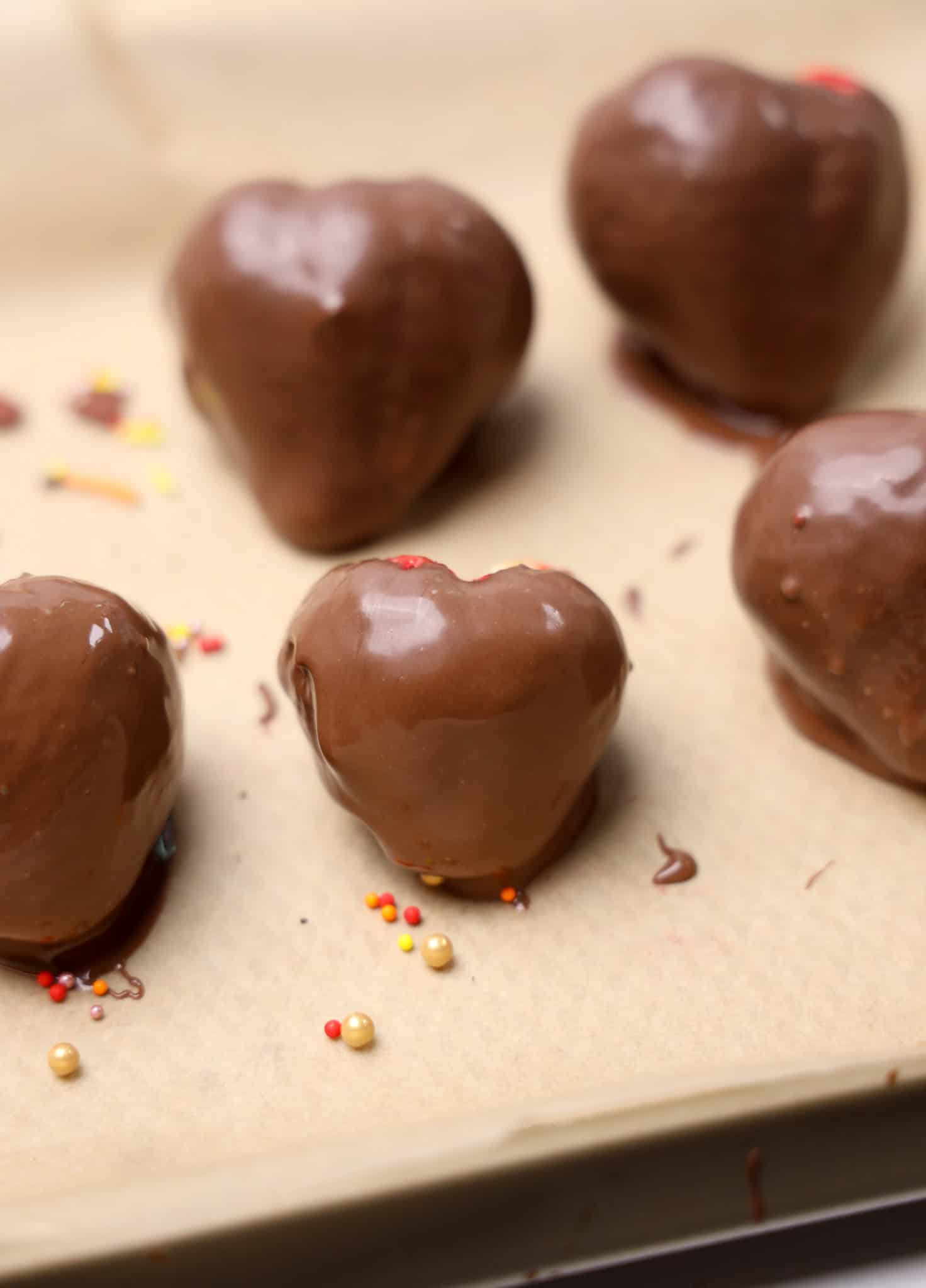 Heart-shaped treats coated in chocolate, topped with colorful sprinkles, these chocolate strawberries rest on parchment paper for a sweet finishing touch.