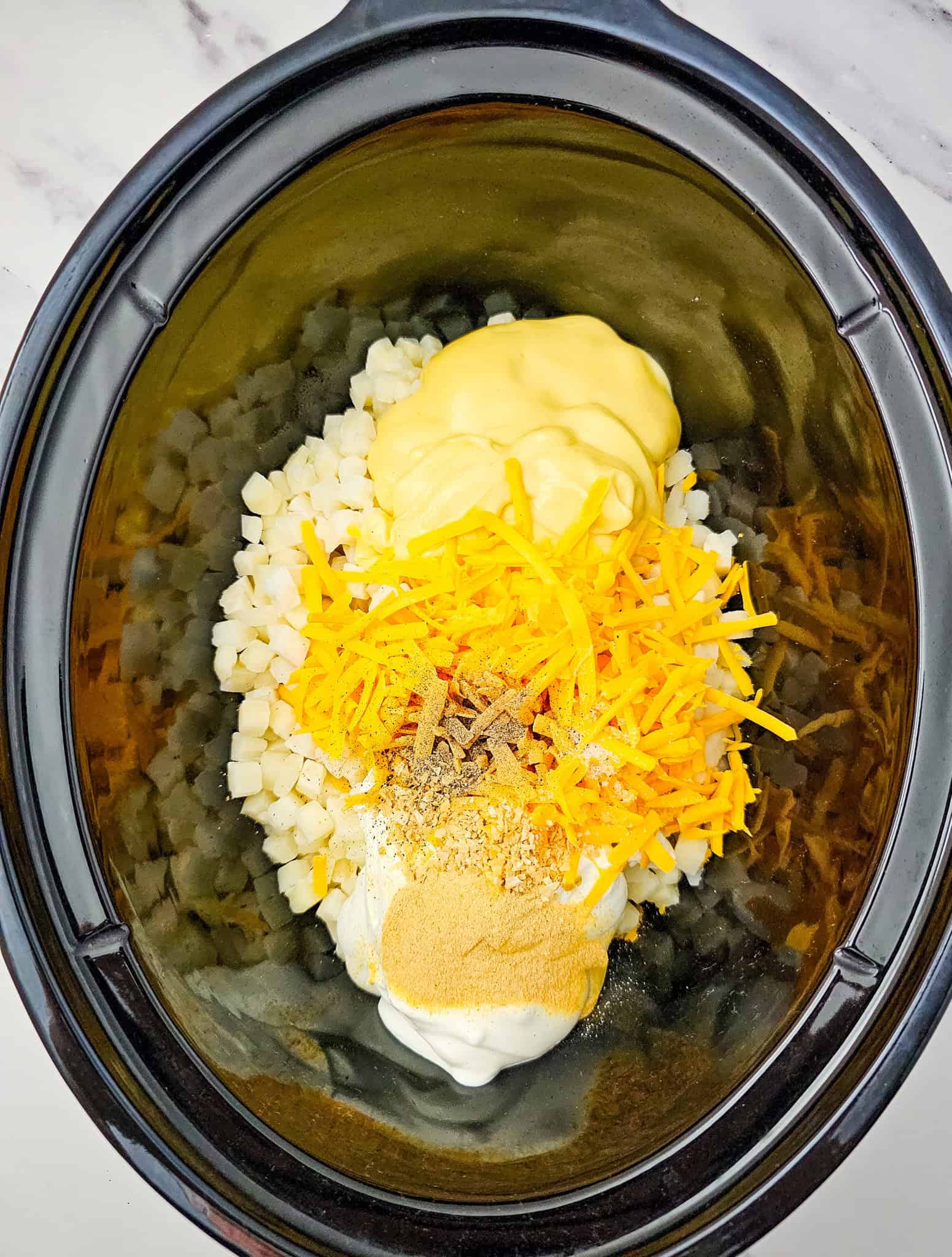 Ingredients including shredded cheese, seasonings, and creamy sauces in a Crockpot, ready to be mixed for delicious Crockpot Cheesy Potatoes.