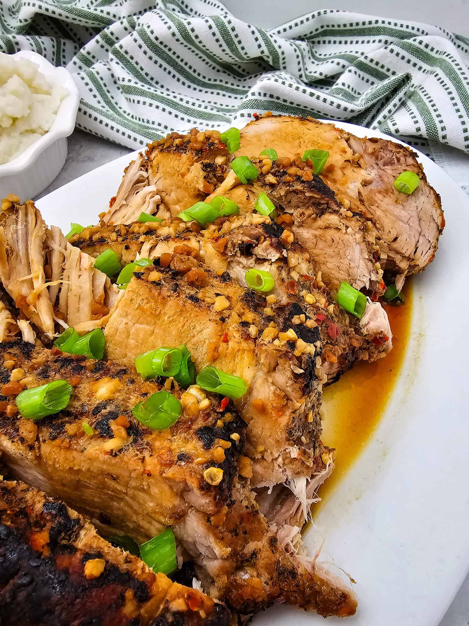 Sliced Honey Garlic Pork Roast garnished with chopped green onions on a white plate, with mashed potatoes in the background.