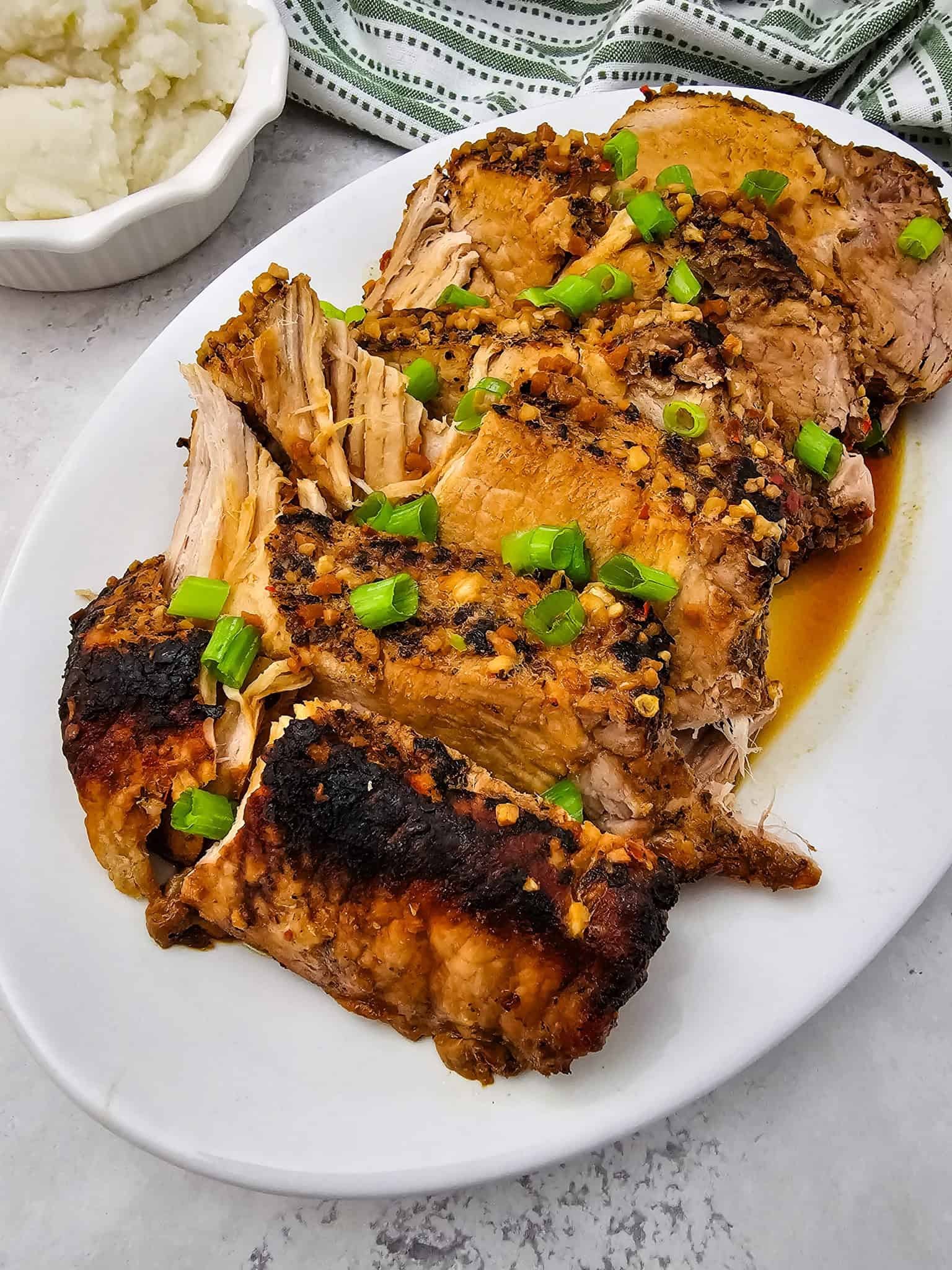 Honey Garlic Pork Roast, slow-cooked in a Crockpot, sliced and seasoned, garnished with chopped green onions on a white plate, served with mashed potatoes.